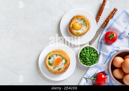 Gebackene Brötchen gefüllt mit Eiern und Speck auf Tellern auf hellem Hintergrund. Frühstückseier. Draufsicht mit Kopierbereich. Stockfoto