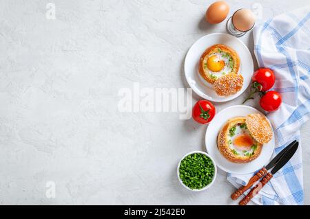 Gebackene Brötchen gefüllt mit Eiern und Speck auf Tellern auf hellem Hintergrund. Frühstückseier. Draufsicht mit Kopierbereich. Stockfoto