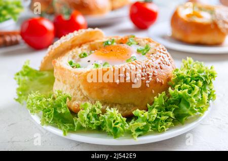 Frühstückseier. Gebackene Brötchen gefüllt mit Eiern und Speck und frischen Kräutern auf Tellern auf hellem Hintergrund. Nahaufnahme Stockfoto