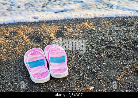 Pinke Kinderschuhe an einem Kiesstrand Stockfoto