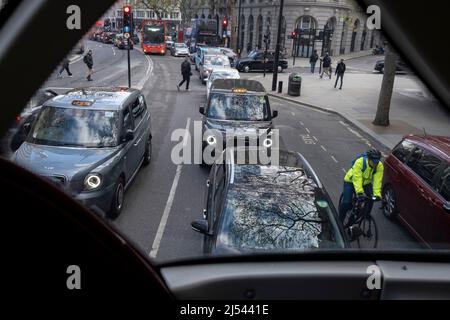 Fußgänger überqueren die Straße, und ein Radfahrer kommt an Autos und Taxis vorbei, die sich in die Ferne strecken, gesehen vom Oberdeck eines Londoner Busses in Aldwych am 13.. April 2022 in London, England. Stockfoto