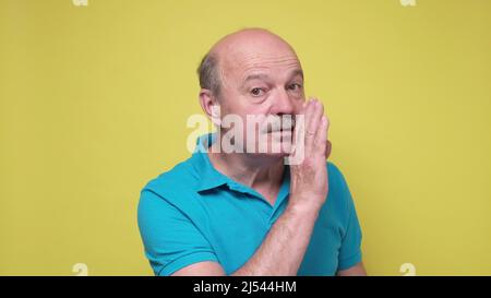 Älterer, gutaussehender Mann, der die Hand am Mund hält und ein Geheimnis oder Gerücht erzählt und es der Kamera zuflüstert. Studioaufnahme Stockfoto