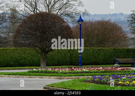 Landschaftlich reizvolle städtische Einrichtungen (helle Bettblumen an gepflegten definierten Grenzen, Wege, Sitzbank) - Lister Park, Bradford, England, Großbritannien. Stockfoto