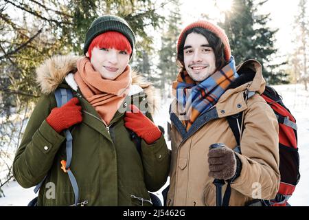 Porträt eines jungen, eleganten Kaukasierers mit Rucksäcken, der am Wintertag irgendwo in den Bergen unterwegs ist und dabei die Kamera anschaut Stockfoto