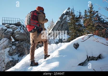 Nicht wiederzuerkennen stilvoller junger Mann in warmer Kleidung und Rucksack, der am Wintertag in den Bergen wandern will Stockfoto