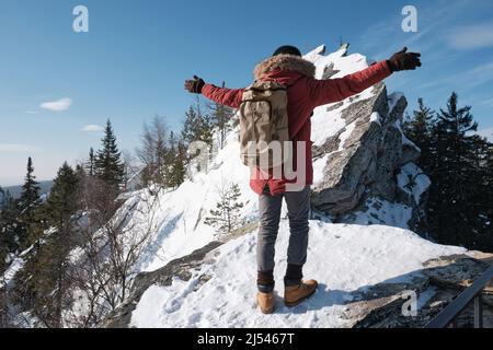 Nicht erkennbarer junger Mann mit warmer Kleidung und Rucksack, der in Bergen unterwegs ist und mit weit geöffneten Armen steht Stockfoto