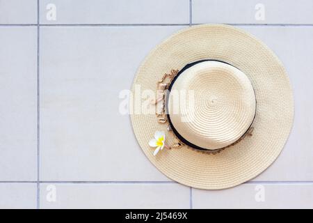 Sommerstrand Strohhut mit einer Halskette mit Muscheln und Perlen und die Plumeria Blume auf dem Fliesenboden, Draufsicht. Das Konzept der Sommerferien und Stockfoto