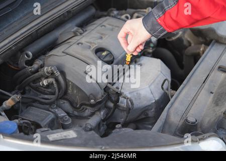 Der Servicetechniker nimmt einen Messstab heraus, um den Ölstand im Automotor zu überprüfen. Stockfoto