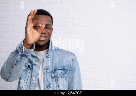 Portrait junger hübscher afrikanischer schwarzer Mann, der eine gute Geste in Jeans-Jacke gegen Backstein zeigt, mit einer Wand im Freien mit Copyspace. Stockfoto