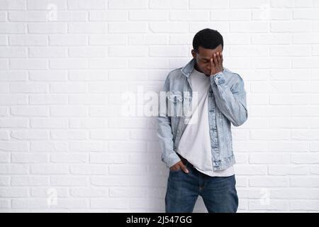 Portrait junger verärgerter afrikanischer schwarzer Mann, der Jeansjacke an Backstein trägt, mit einer Wand im Freien mit Copyspace. Stockfoto