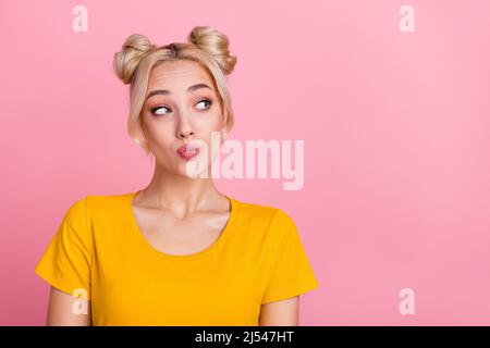 Foto von flirty Millennial blonde Brötchen Frisur Dame aussehen Werbung tragen gelbe T-Shirt isoliert auf rosa Hintergrund Stockfoto