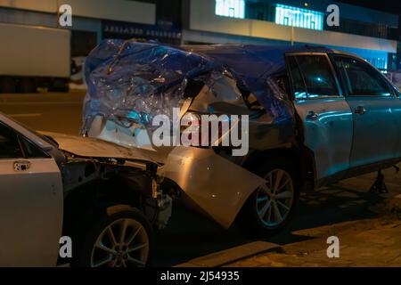 Verbeultes, gebrochenes graues Auto auf der Straße in der Stadt in der Nacht Stockfoto