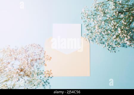 Umschlag und leeres Blatt auf blauem Hintergrund mit Gypsophila-Blüten im Sonnenlicht. Draufsicht, flaches Lay, Mockup Stockfoto