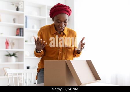 Erstaunt afroamerikanische Frau öffnen Lieferbox zu Hause Stockfoto