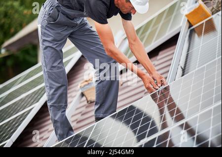 Mann Techniker Montage Photovoltaik-Solarmodule auf Dach des Hauses. Beschnittene Ansicht des Arbeiters, der Solarpanel-System im Freien installiert. Konzept der alternativen und erneuerbaren Energien. Stockfoto