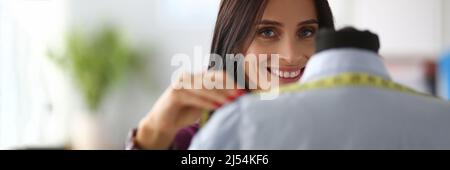 Lächelnde Modedesignerin nimmt Messungen mit einem Zentimeter von Schaufensterpuppe Stockfoto