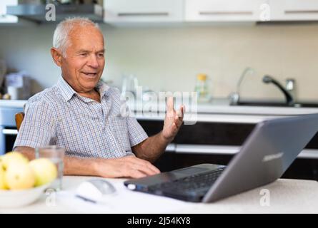 Älterer Mann, der am Tisch sitzt und über das Internet spricht Stockfoto