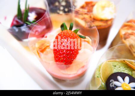 Erdbeer-Käsekuchen mit frischen Erdbeeren auf der Oberseite und verschiedenen Geschmacksrichtungen von Käsekuchen auf dem weißen Holztisch Stockfoto