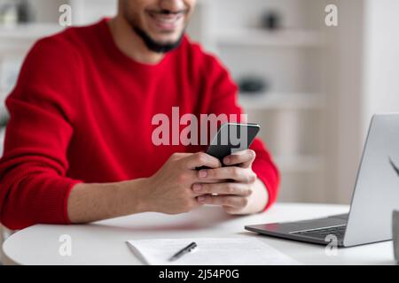 Happy Millennial arabisch Geschäftsmann mit Bart tippen auf Smartphone und Laptop im Home Office Innenraum, abgeschnitten Stockfoto