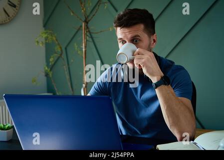 Überraschender Mann, der auf den Laptop-Bildschirm schaute Stockfoto