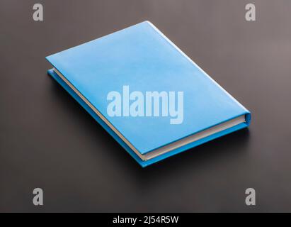 Eine unbeschriftete, blaue Notebook-Hardcover auf schwarzer Oberfläche Stockfoto