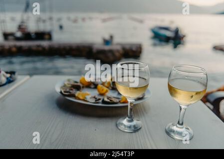 Frisch gefangenen Austern auf einem Teller und Weingläsern. Restaurant am Ufer der Bucht von Kotor in der Nähe der Austernfarm, Montenegro. Meeresfrüchte. Wunderschön Stockfoto