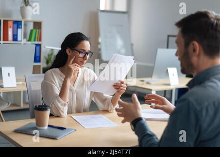 Personalmanager, der mit dem Kandidaten für eine offene Stelle kommuniziert, liest während des Vorstellungsgesprächs im Büro den Lebenslauf Stockfoto
