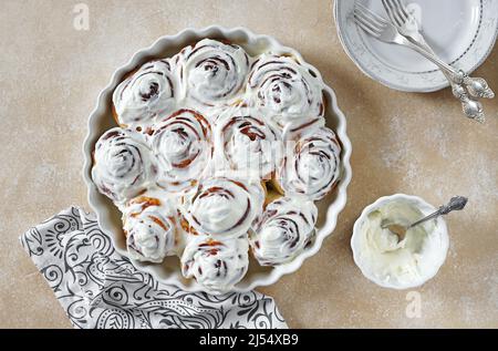 Zimtrollen oder Zimtbrötchen, hausgemachte süße traditionelle Dessertbrötchen mit weißer Sahnesauce auf dem Bienchen-Hintergrund, Kopierraum. Draufsicht Stockfoto