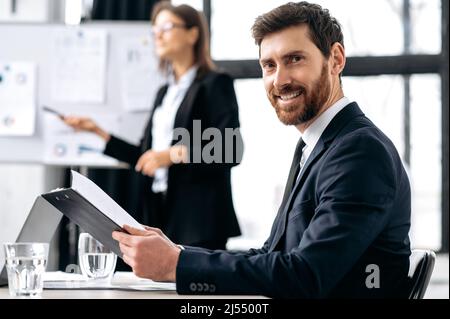 Erfolgreicher Geschäftsmann, CEO des Unternehmens, sitzt während eines Brainstorms im Büro, blickt auf die Kamera und lächelt. Porträt eines attraktiven kaukasischen männlichen Geschäftsführers in formeller Klage beim Briefing Meeting Stockfoto
