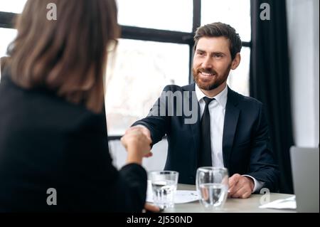 Hände schütteln, Vereinbarungen treffen, Vereinbarungen treffen. Kaukasische einflussreiche attraktive erfolgreiche Geschäftsmann, Entwicklungs-Chef, ceo-Unternehmen, schüttelt die Hände mit weiblichen Kollegen in modernen Büro, lächeln einander an Stockfoto