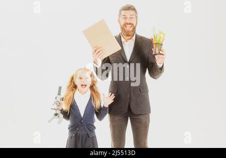 Grundschüler mit aufgeregter Lehrerin im Studio, isoliert. Lehrerin mit Buch und Schulmädchen mit Schulbedarf isoliert auf weißem Hintergrund. Stockfoto