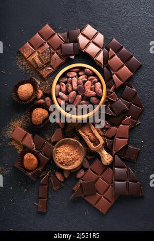 Kakao aus Schokoladenbohne. Zusammensetzung aus Kakaopulver, Bohnenkakaobarren und Stücken verschiedener Milch und dunkler Schokolade auf schwarzem Hintergrund. Backen Chocola Stockfoto