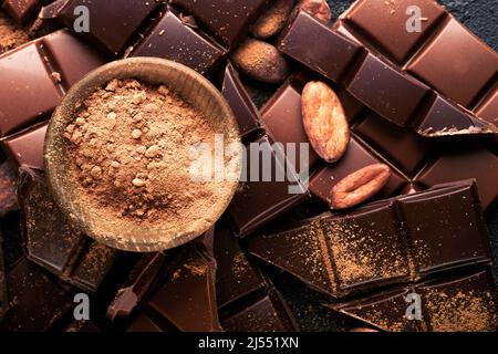 Schokolade und Kakaopulver. Zusammensetzung aus Kakaopulver, geriebenen und Bohnenkakaobars und Stücken verschiedener Milch und dunkler Schokolade auf schwarzem Backgroun Stockfoto