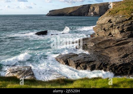 Zwei junge Männer in der Ferne fischen von Felsen in Trebarwith Strand, North Cornwall, Großbritannien. Stockfoto