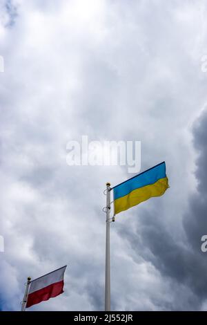 Polnische und ukrainische Flaggen wehen vor dem Hintergrund des wolkigen, dramatischen Himmels. Foto am Tag, Himmel voller Wolken. Stockfoto