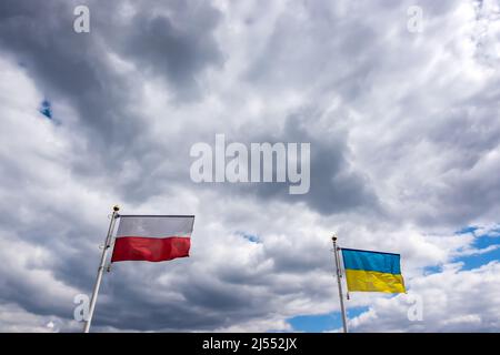 Polnische und ukrainische Flaggen wehen vor dem Hintergrund des wolkigen, dramatischen Himmels. Foto am Tag, Himmel voller Wolken. Stockfoto