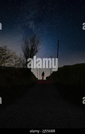 Eine stary Night und ein Straßenradfahrer, der auf der berühmten Clinkham Road mit Kopfsteinpflaster, Great Harwood, Lancashire, Großbritannien, unterwegs ist. Stockfoto