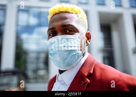 Mulatto latin Geschäftsmann in der marsala Jacke setzen auf Maske Prävention Luftverschmutzung in großen sity im Freien Büro Hintergrund Stockfoto