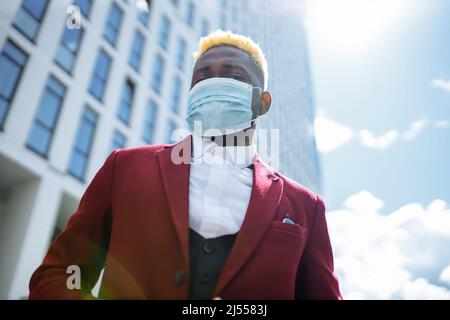 Mulatto latin Geschäftsmann in der marsala Jacke setzen auf Maske Prävention Luftverschmutzung in großen sity im Freien Büro Hintergrund Stockfoto