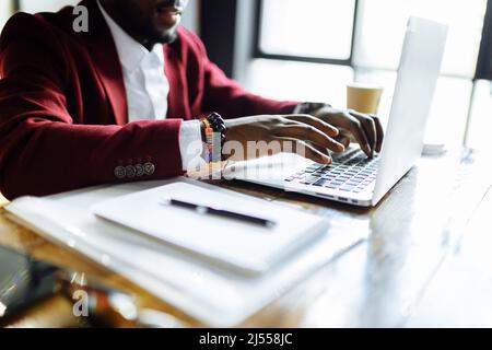 Lächelnder Geschäftsmann in einer marsala-Jacke, der im Büro am Laptop arbeitet Stockfoto