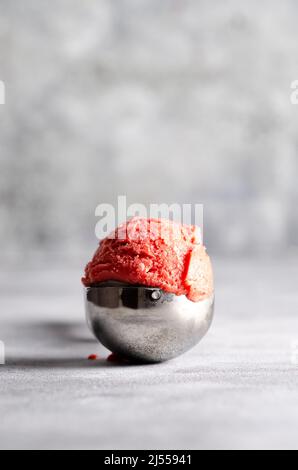 Eine Schaufel Erdbeereis in einer Metallkugel auf grauem Hintergrund. Stockfoto