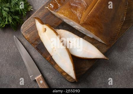 Geräucherte Heilbutt-Scheiben auf braunem Hintergrund. Blick von oben. Stockfoto