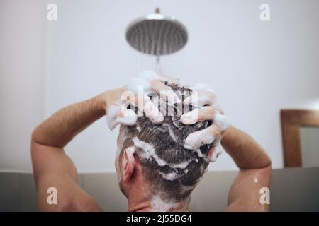 Rückansicht des Mannes beim Waschen der Haare in der Dusche im Badezimmer. Nasse Haare mit Schaum von Shampoo. Stockfoto