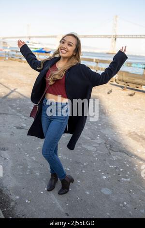 Junge Frau tanzend fröhlich am Pier mit der Oakland Bay Bridge im Hintergrund | Lifestyle Local Tourism Stockfoto