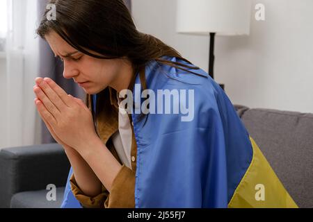 Nahaufnahme der hoffnungsvollen traurigen jungen Frau mit Flagge der Ukraine bedeckt, beten für ukrainische Menschen und Verteidiger, verärgert Brünette Mädchen allein auf cou sitzen Stockfoto