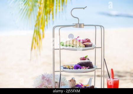 Nachmittagstee am tropischen Sandstrand mit blauem Meer und Palmenblatt im Hintergrund Stockfoto