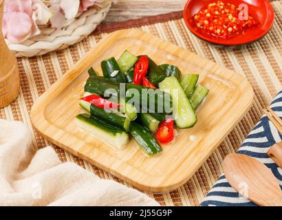 Kalte Gurke mit rotem Chili in einer Holzschale mit Löffel und Essstäbchen isoliert auf Matte Seitenansicht auf Holztisch taiwan Essen Stockfoto