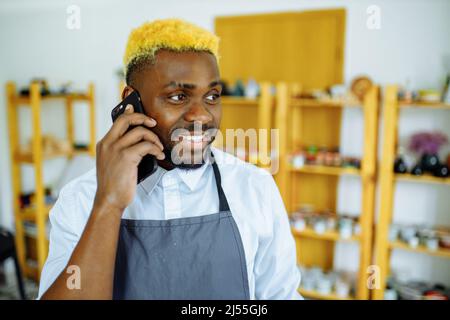 afro männlicher Töpfer, der in seinem Studio telefoniert Stockfoto