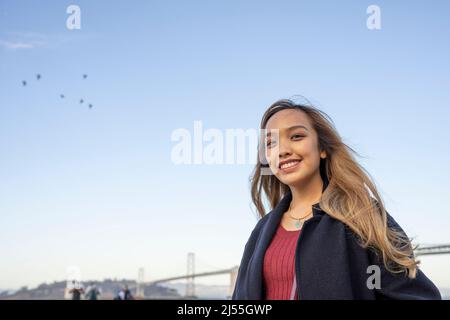 Glückliche junge Frau mit einem Vogelschwarm und der Oakland Bay Bridge im Hintergrund | Lifestyle Local Travel Stockfoto