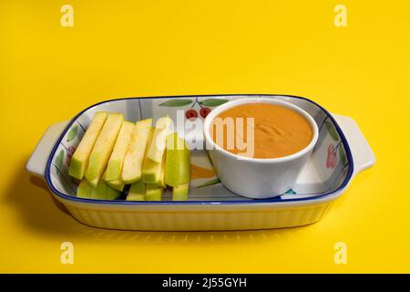 Grüne Apfelscheiben und Erdnussbutter in einer Tasse. Gelber Hintergrund. Stockfoto